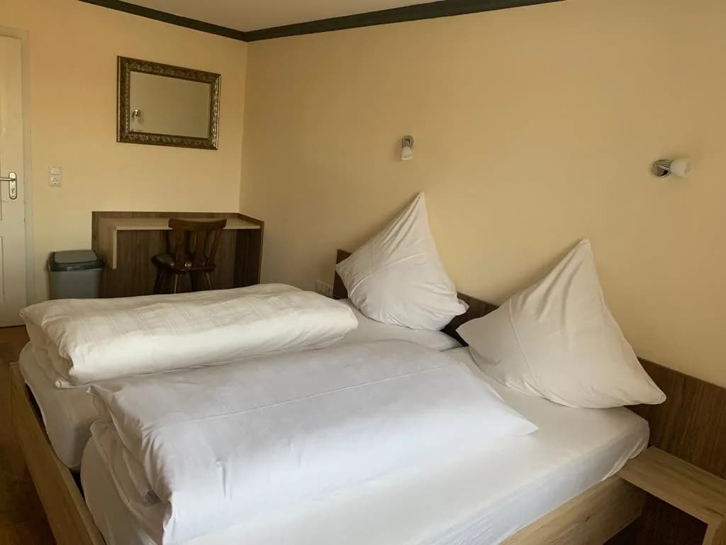 Hell eingerichtetes Zimmer mit Bett, Schreibtisch und Spiegel